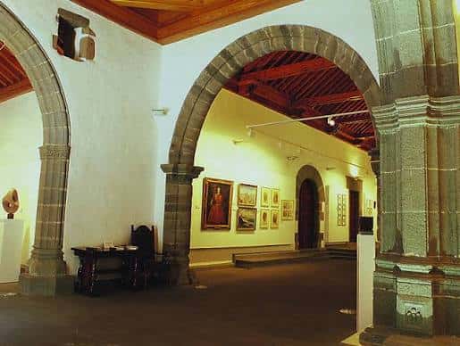 Interior de la Iglesia Hospitalaria de San Pedro Mártir de Verona mostrando arcos de piedra y exposición de arte