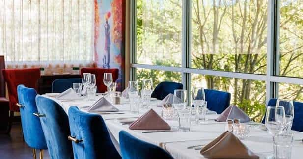 Sala de eventos con mesas largas, sillas azules y grandes ventanales