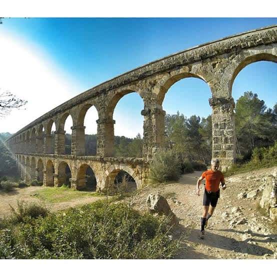 Corredor deportivo pasando junto al Puente del Diablo bajo un cielo azul despejado