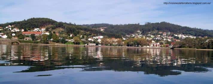 Panorámica de la costa de A Cabana con casas y vegetación reflejadas en el agua