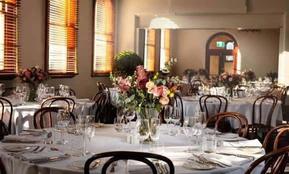 Sala de eventos decorada con mesas, flores y cristalería