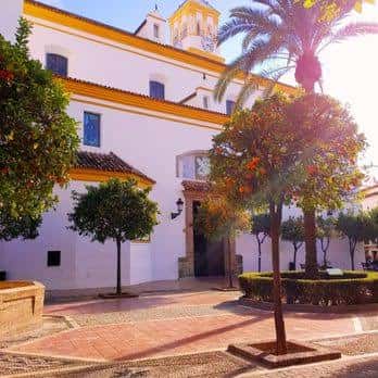 Fachada blanca de la iglesia con detalles amarillos y palmeras al atardecer