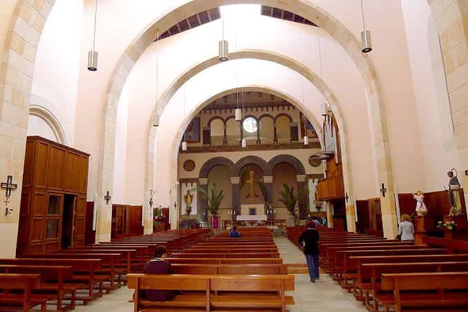 Interior de la iglesia con naves, bancos de madera y altar central