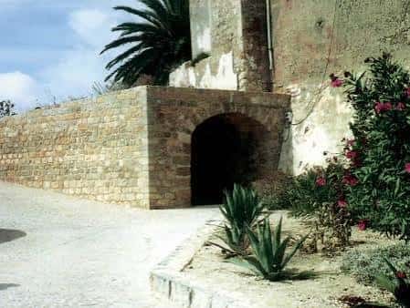 Entrada arqueada en la muralla con vegetación mediterránea