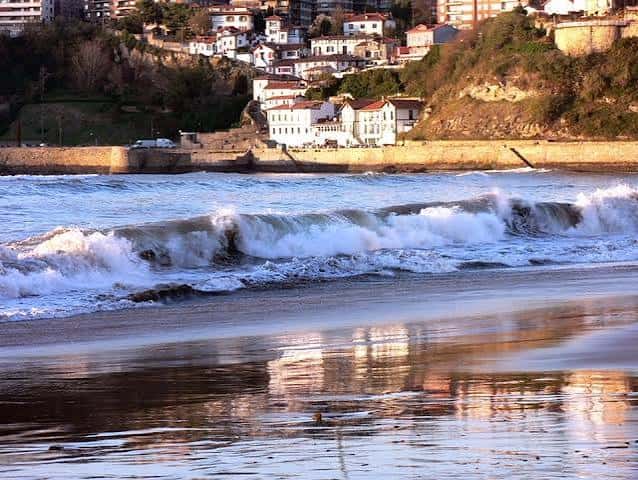 Olas rompiendo en la Playa de Ereaga con casas en la colina de fondo