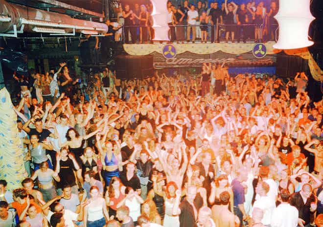 Fiesta multitudinaria en el interior de Amnesia Ibiza con luces cálidas y público bailando