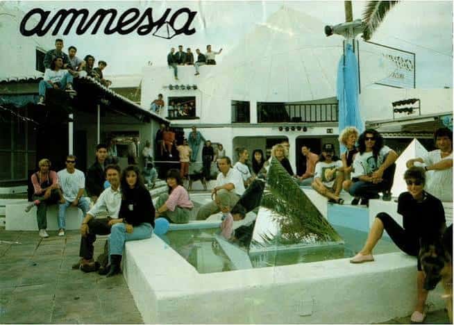 Vista exterior histórica de Amnesia Ibiza con personas relajadas junto a una fuente y estructura blanca