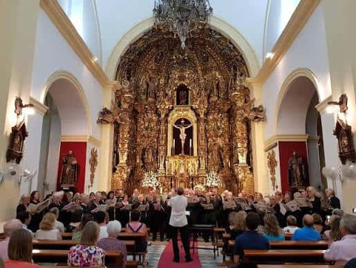 Interior de la iglesia con coro y retablo mayor dorado durante un evento