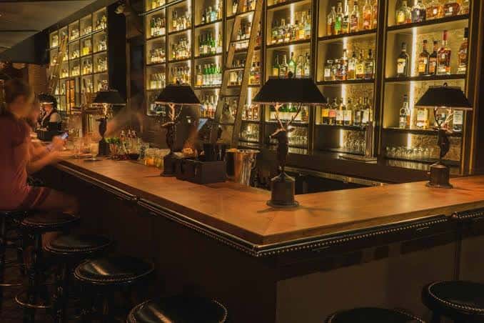 Vista del interior del bar con estanterías iluminadas de botellas y barra de madera