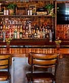 Vista del mostrador del bar con taburetes de madera y estantería de licores