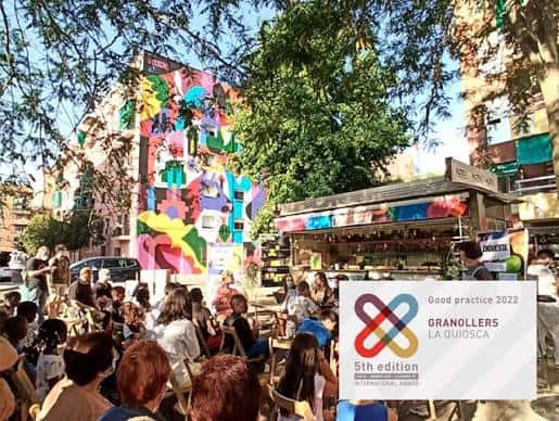 Vista exterior de La Quiosca con murales coloridos y público reunido