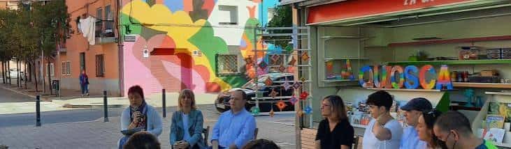 Panel de personas frente a La Quiosca con fondo de murales artísticos