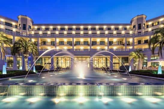 Fachada iluminada del hotel al atardecer con fuente decorativa en primer plano