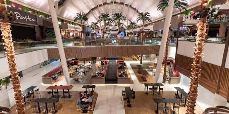 Vista panorámica del interior del centro comercial con palmeras y zonas de restauración