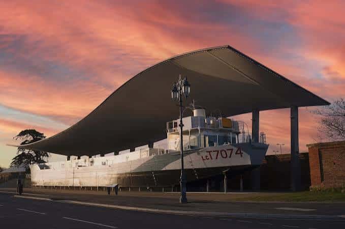 El barco LCT 7074 al atardecer con cielo rosado y estructura de protección