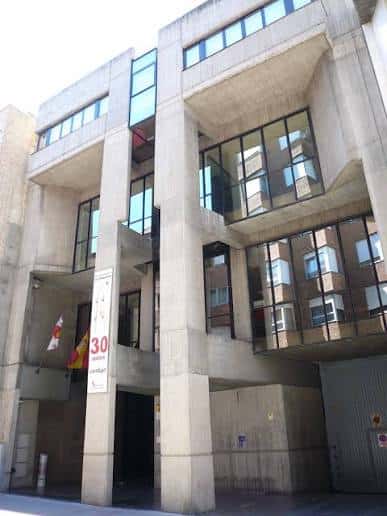 Vista frontal del edificio de la biblioteca con columnas de hormigón y banderas