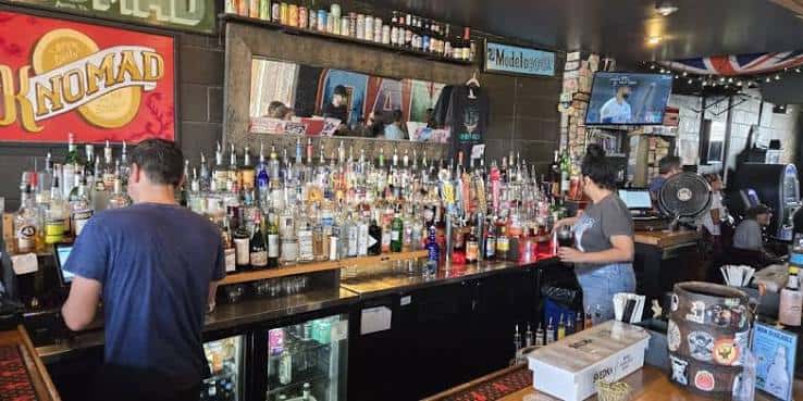 Interior del bar mostrando la barra con múltiples botellas y clientes
