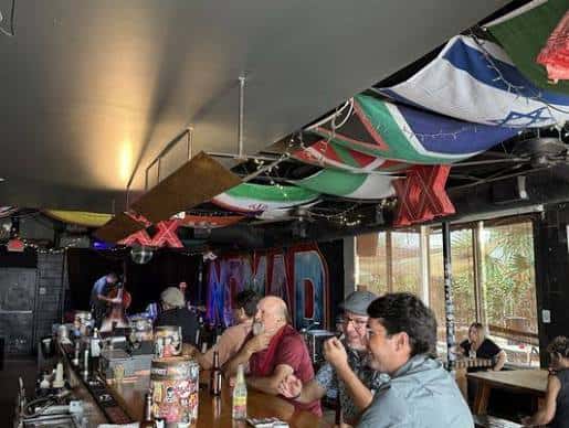Ambiente interior del Knomad Bar con banderas colgando y clientes sentados