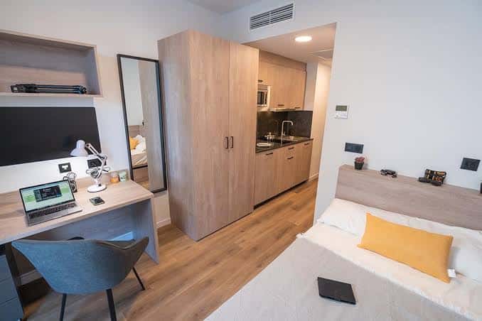 Habitación individual con cama, escritorio y cocina integrada