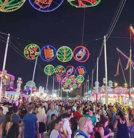 Ambiente festivo nocturno en la feria con luces decorativas y multitud de visitantes