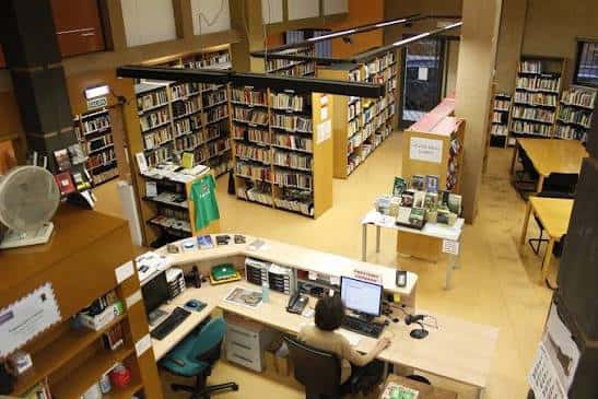 Vista interior de la sala principal de la Biblioteca Contrueces con estanterías y mostrador de atención al público