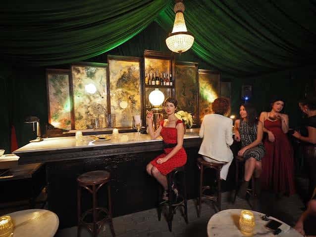 Bar con decoración verde y clientes disfrutando de bebidas