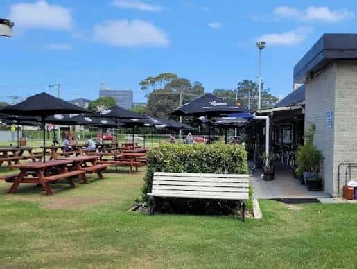 Área exterior con mesas de picnic bajo sombrillas y césped, ideal para eventos al aire libre