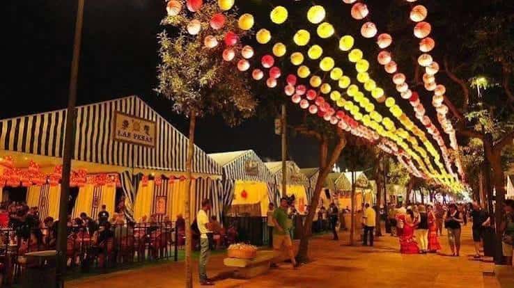 Pasillo de casetas con toldos a rayas y farolillos colgantes durante la feria