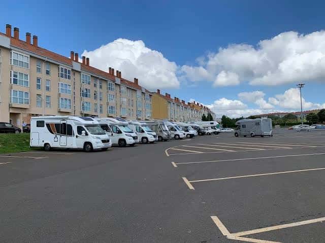 Vista general del parking de autocaravanas Salgueiriños con vehículos estacionados y edificios residenciales al fondo