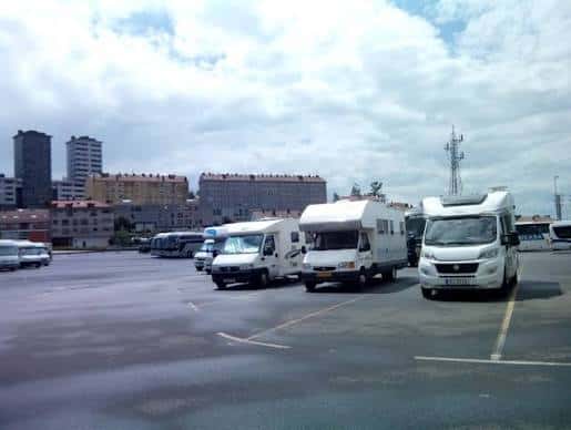 Parking de autocaravanas con vista urbana al fondo y varios vehículos estacionados en fila