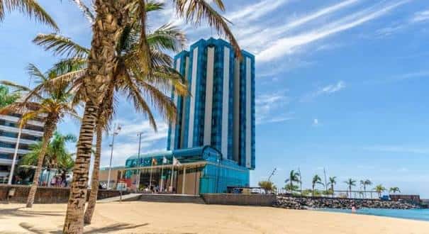 Fachada del hotel con palmeras y acceso a la playa en un día soleado