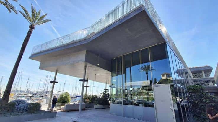 Vista exterior moderna del Club de Mar con fachada de cristal y palmeras