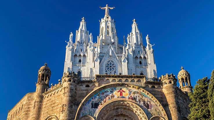 Vista frontal del templo bajo un cielo azul intenso, destacando su arquitectura neogótica y el mosaico del arco central