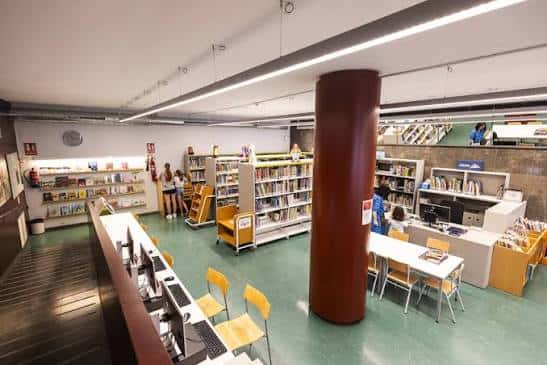Área de lectura con mesas, sillas y columnas decorativas en el interior de la biblioteca