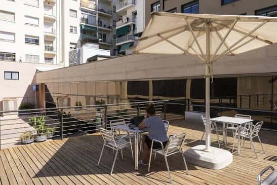 Terraza exterior de la biblioteca con mesas, sombrillas y vista a edificios residenciales