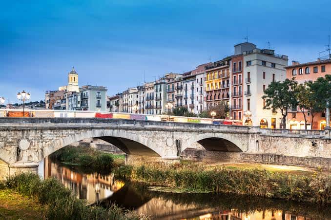 Vista panorámica del Pont de Pedra al atardecer con edificios iluminados y reflejos en el río