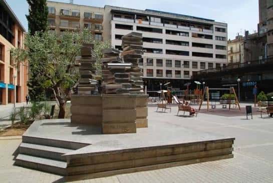 Plaza Josep Pla con escultura de libros y área de juegos infantiles
