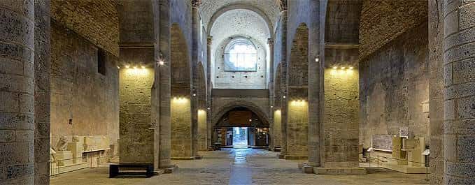 Nave central del claustro románico con columnas de piedra y bóvedas iluminadas