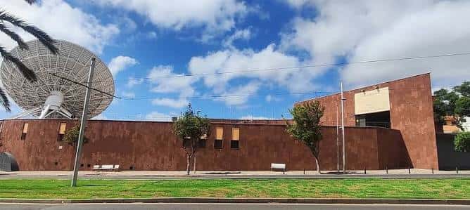 Exterior de Finca España con antena satelital y muro de ladrillo bajo cielo nublado