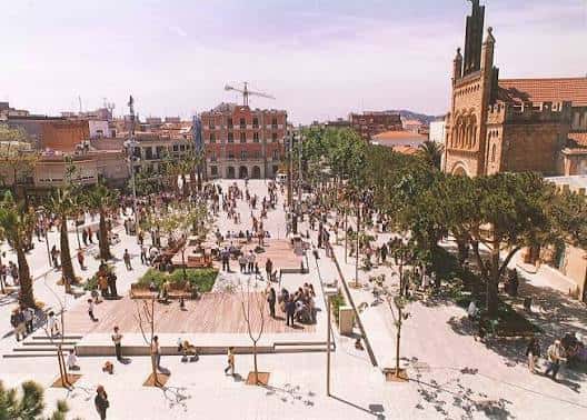 Vista panorámica de la Plaça de l'Església con la iglesia al fondo y personas disfrutando del espacio público