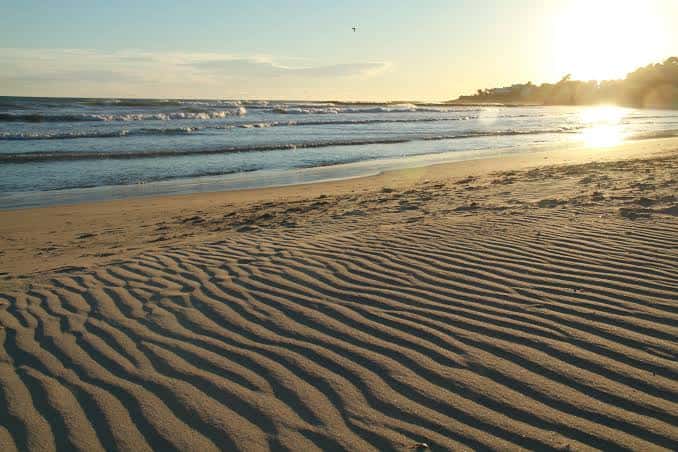 Atardecer en la arena de la playa con olas suaves y reflejos dorados