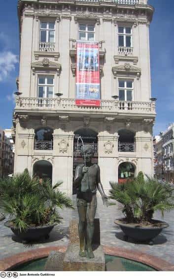 Plaza con el monumento al Icue y fachada del edificio con cartel publicitario