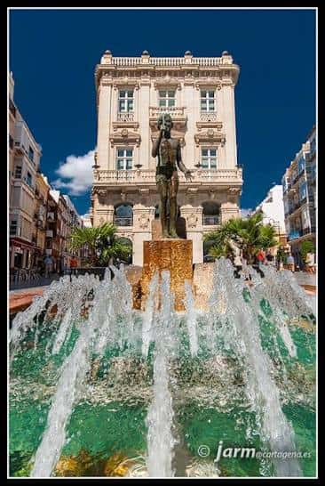 Vista frontal del Monumento al Icue con fuente en primer plano y edificio histórico de fondo