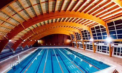Piscina cubierta interior con techo de madera curvado y carriles de natación