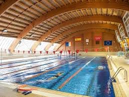 Piscina olímpica cubierta con banderas de competición y estructura de madera