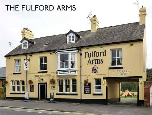 Vista frontal del Fulford Arms con fachada amarilla, letrero del nombre y entrada al aparcamiento trasero