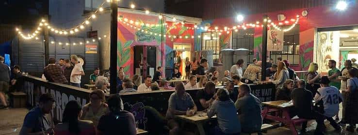Vista nocturna del patio exterior de la cervecería con luces de fiesta y gente socializando
