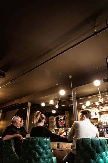 Vista del bar interior con taburetes verdes tapizados y lámparas colgantes modernas