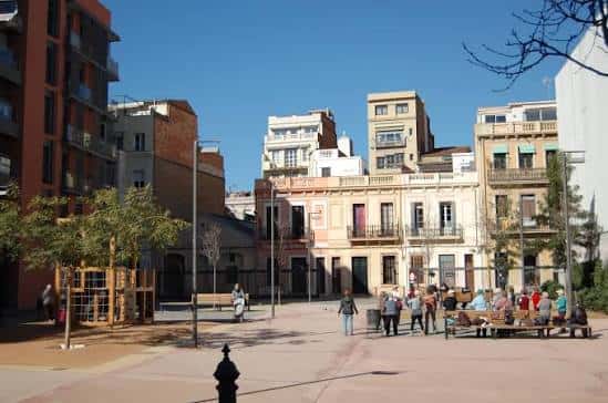 Vista general de la Plaça de les Dones del 36 con edificios históricos y personas disfrutando del espacio