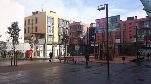 Plaza con áreas de juego infantil y bancos bajo un cielo parcialmente nublado